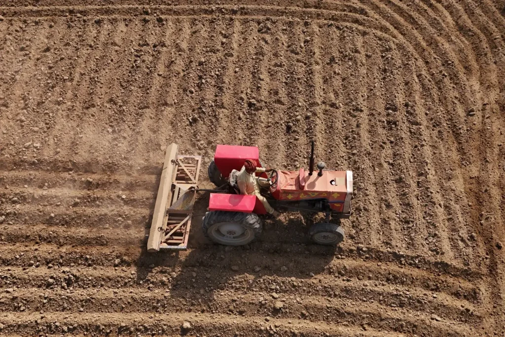 Aerial view of a red tractor ploughing curved furrows.