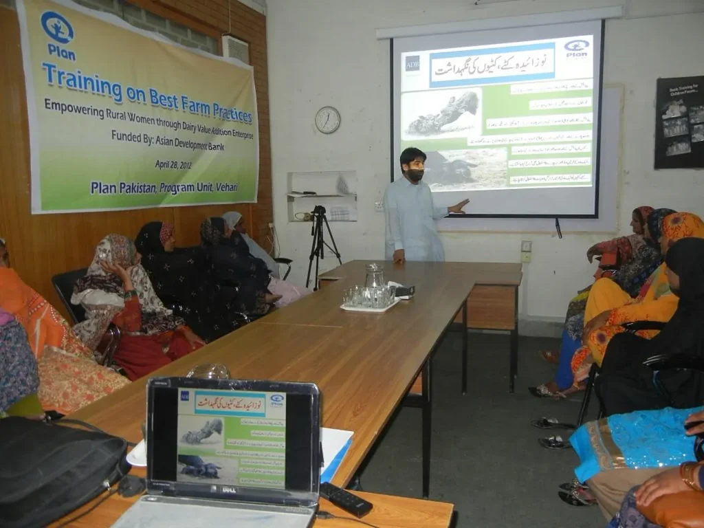A trainer presents a slide on best farm practices to participants seated around a meeting table.