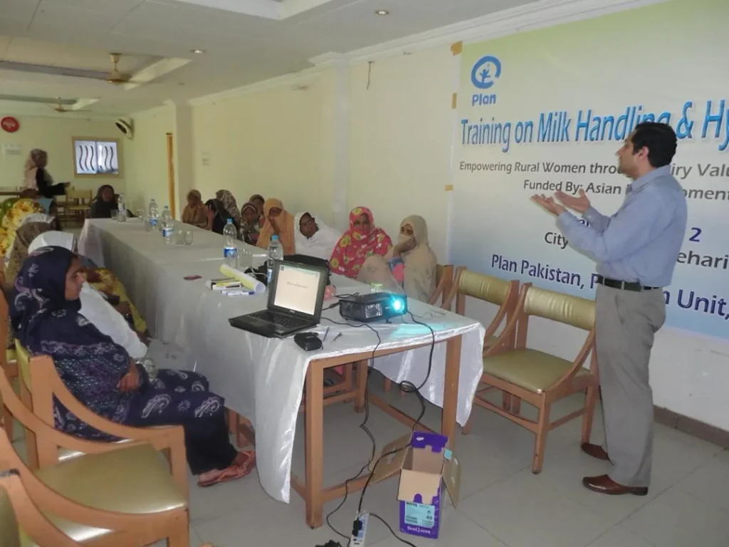 A trainer speaks to seated women participants at a dairy handling and hygiene training.